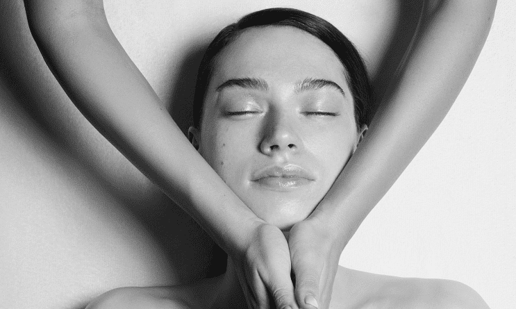 Serene woman with closed eyes, arms encircling her head in a calming, symmetrical pose.