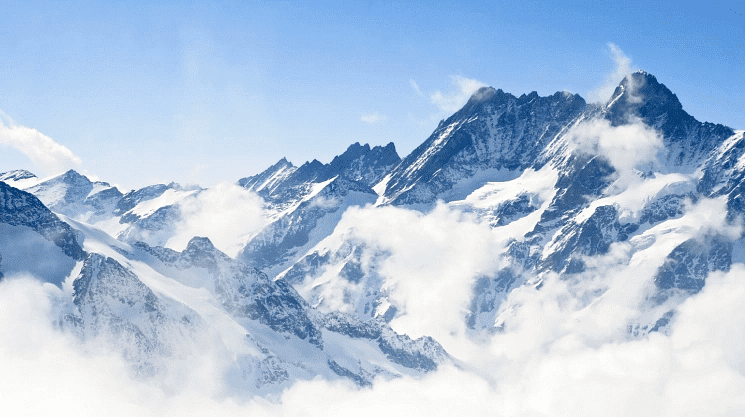 Mountain peaks rising through clouds against a clear blue sky.