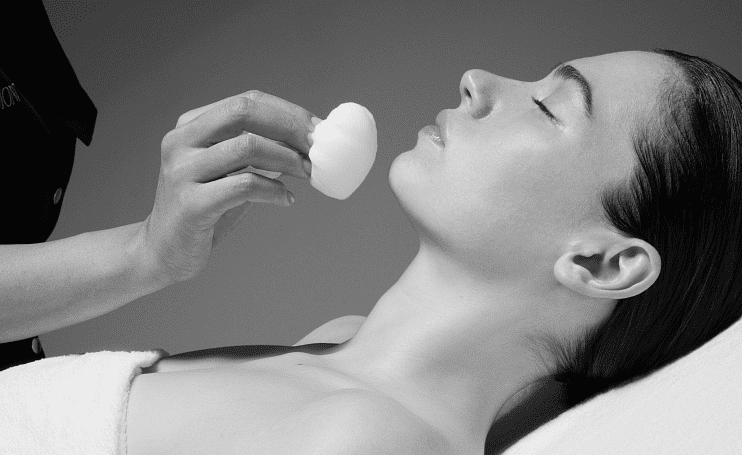 A person receives a facial treatment with a soft sponge in a spa setting.