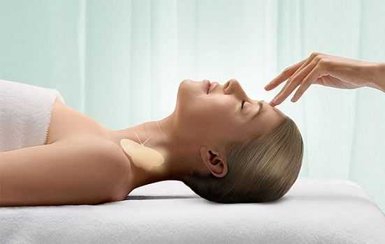 Relaxing spa treatment with a person lying down; hand gently touches their forehead.