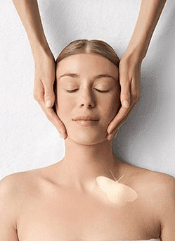 Woman receiving a facial massage with a glowing butterfly on her shoulder.