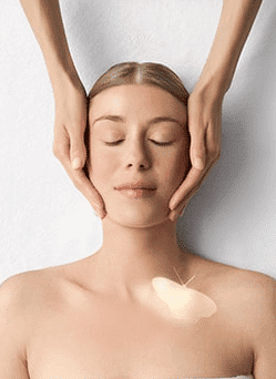 Woman receiving a facial massage with a glowing butterfly on her shoulder.